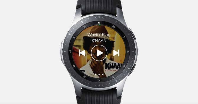 لقطة شاشة لـ Galaxy Watch مع تطبيق Spotify مع عناصر التحكم في الموسيقى وغطاء الألبوم في الخلفية.